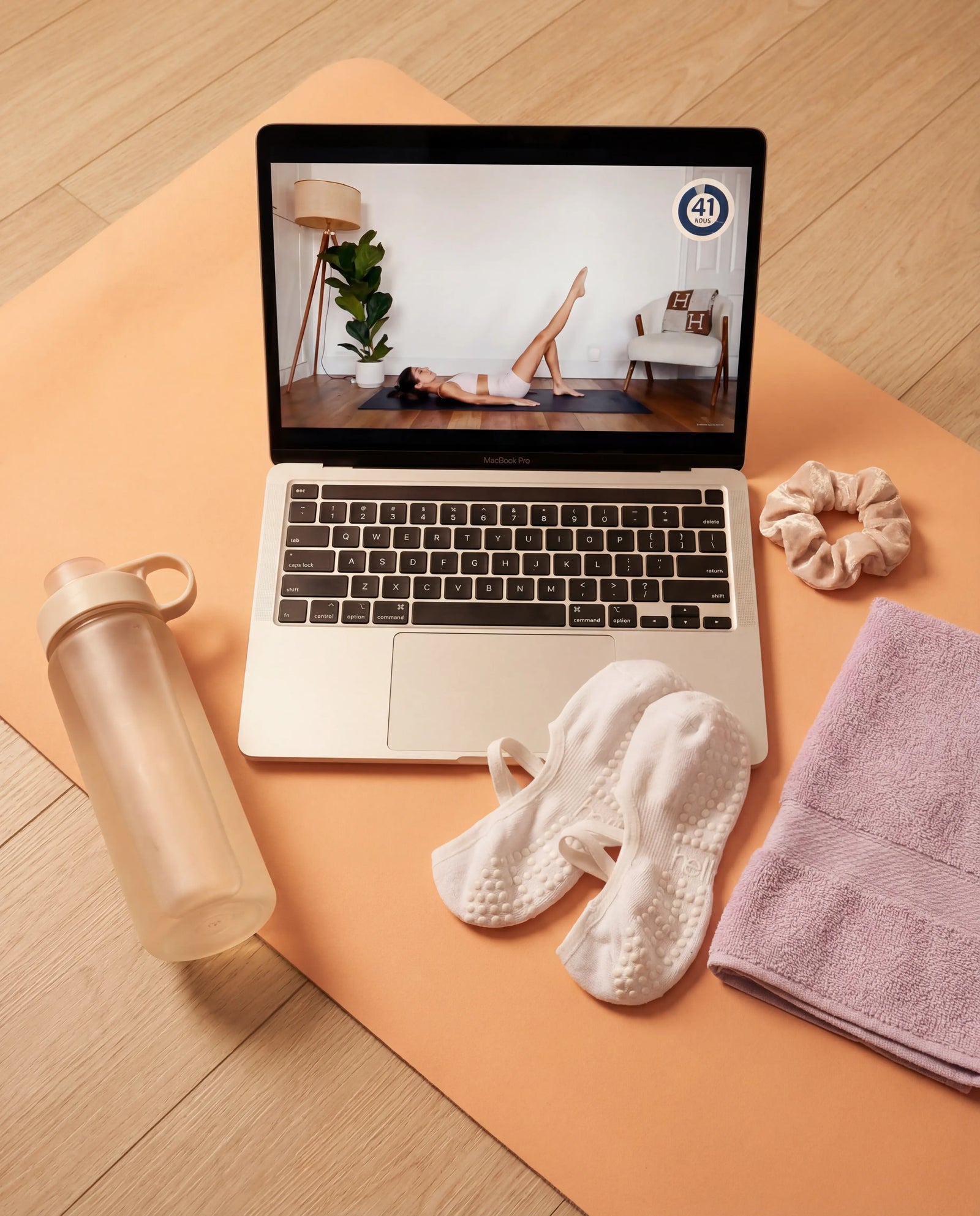 Laptop on a yoga mat with pilates video, water bottle, towel, and grip socks