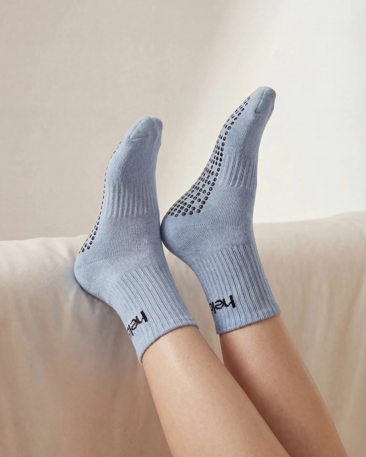 Person wearing light blue socks with black navy grip on a beige couch.