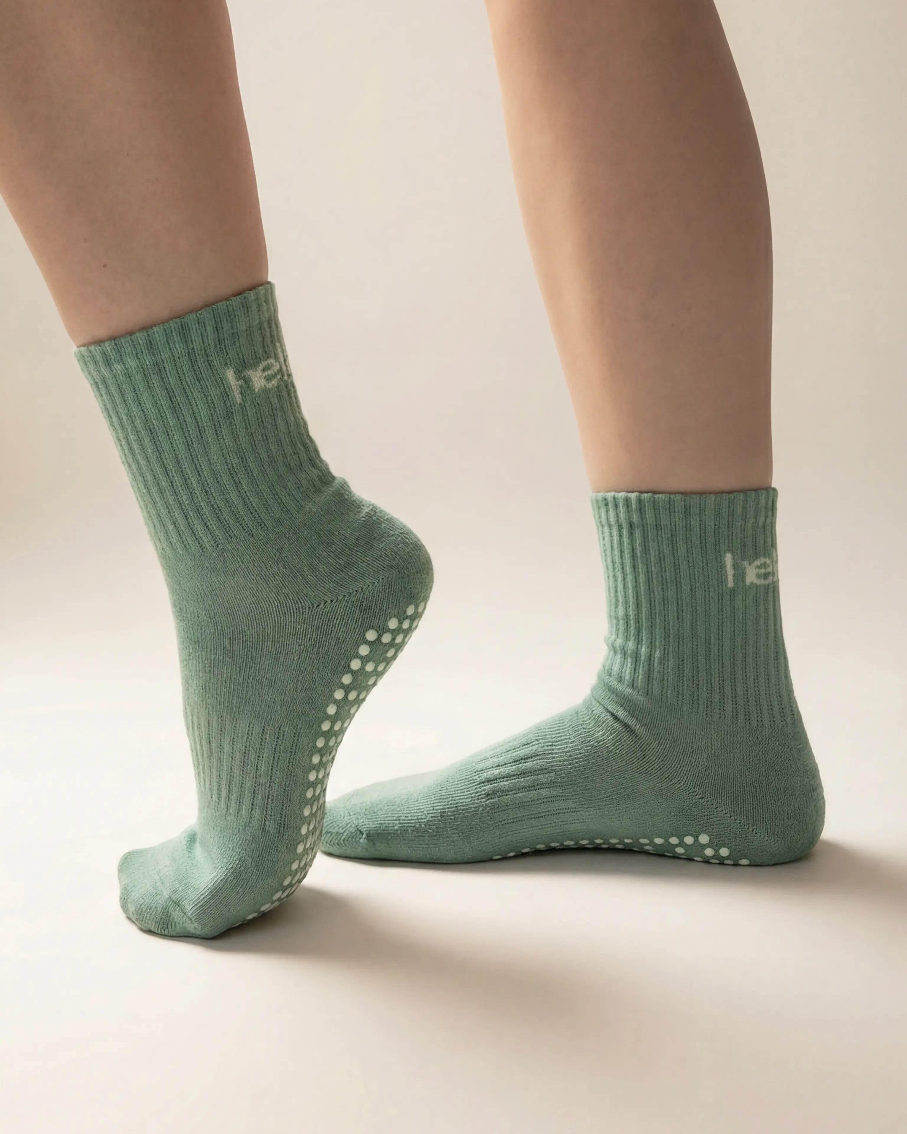 Green socks with non-slip sole worn by a person on a beige background