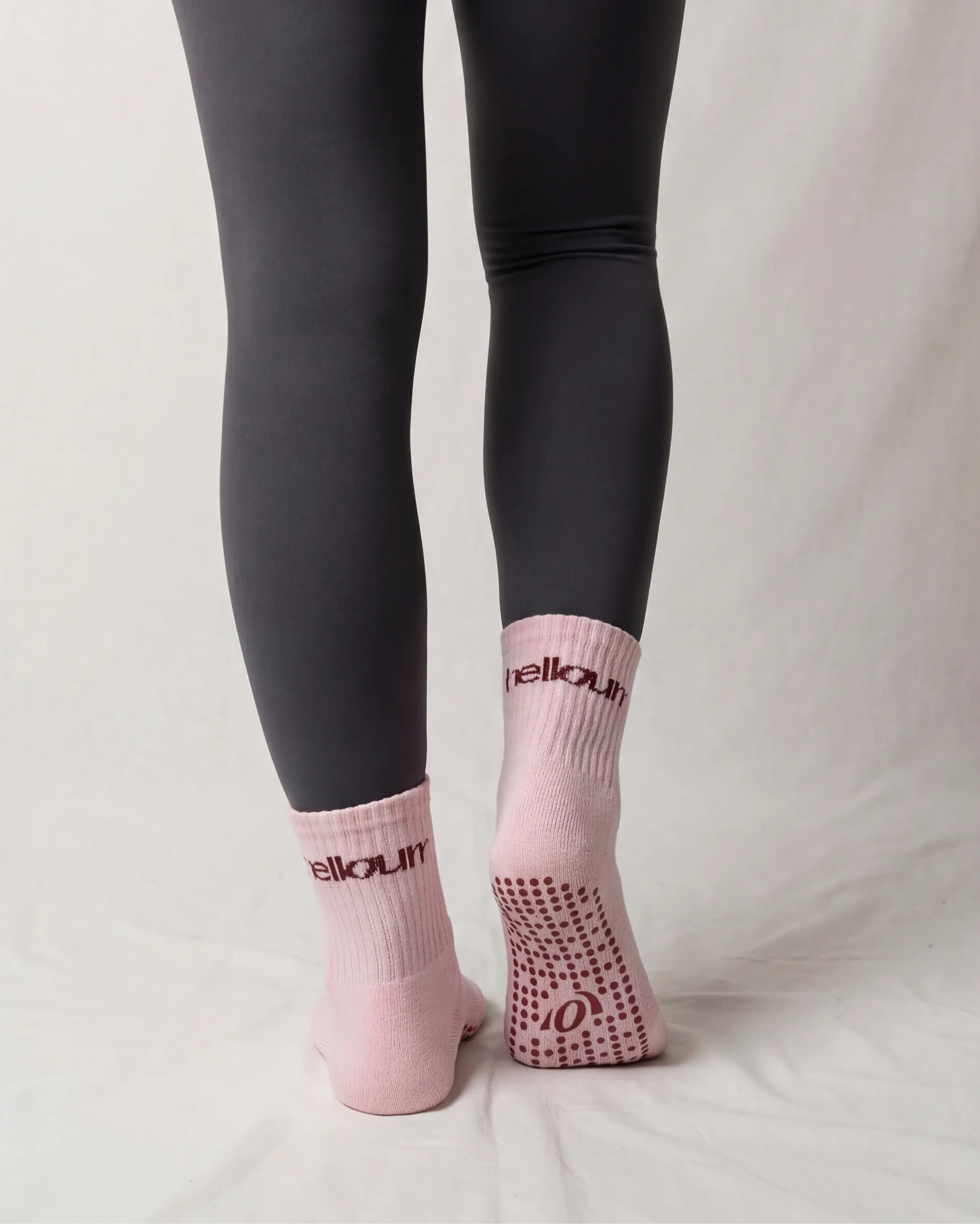 Person wearing black leggings and pink socks with a brand logo on a plain background